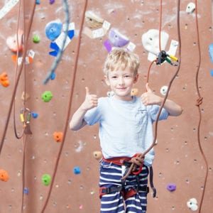 young male climber giving thumbs up while in harness at a climbing gym